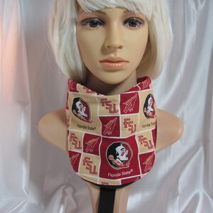 May include: A red and gold neck gaiter with a repeating pattern of the Florida State Seminoles logo, including the Seminole head mascot, the letters FSU, and a stylized arrow. The text "Florida State®" appears on the gaiter.