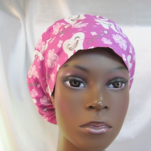 May include: Pink surgical scrub hat with a white tooth and dental tools pattern.