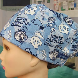 May include: A light blue scrub cap with a repeating pattern of UNC logos, the words "North Carolina," and the UNC mascot. The cap is made of a soft fabric and is designed for medical use.