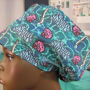 May include: A blue and green surgical scrub hat with a repeated pattern of pink brains, a spinal cord, and the text "Neuro Surgery".