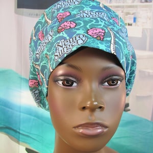 May include: A turquoise blue surgical scrub hat with a white and pink brain pattern. The hat has the text "Neuro Surgery" repeated on it.