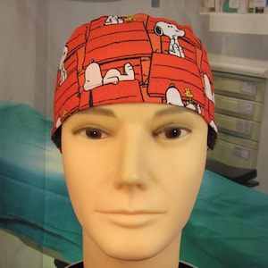 May include: A scrub cap featuring a vibrant red background with a repeating pattern of the white cartoon dog Snoopy lying on top of a red doghouse, accompanied by the small yellow bird Woodstock, designed with a fitted silhouette for head coverage.