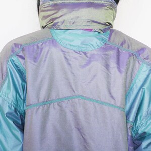 Pu&ograve; includere: Una giacca blu e viola iridescente con colletto alto e chiusura a zip. La giacca ha un design trapuntato ed &egrave; realizzata in un materiale leggero.