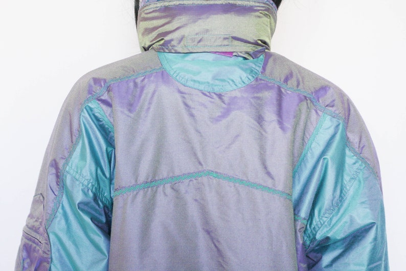 Pu&ograve; includere: Una giacca blu e viola iridescente con colletto alto e chiusura a zip. La giacca ha un design trapuntato ed &egrave; realizzata in un materiale leggero.
