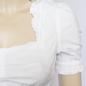 Pu&ograve; includere: Una blusa bianca a maniche corte con scollo a volant.