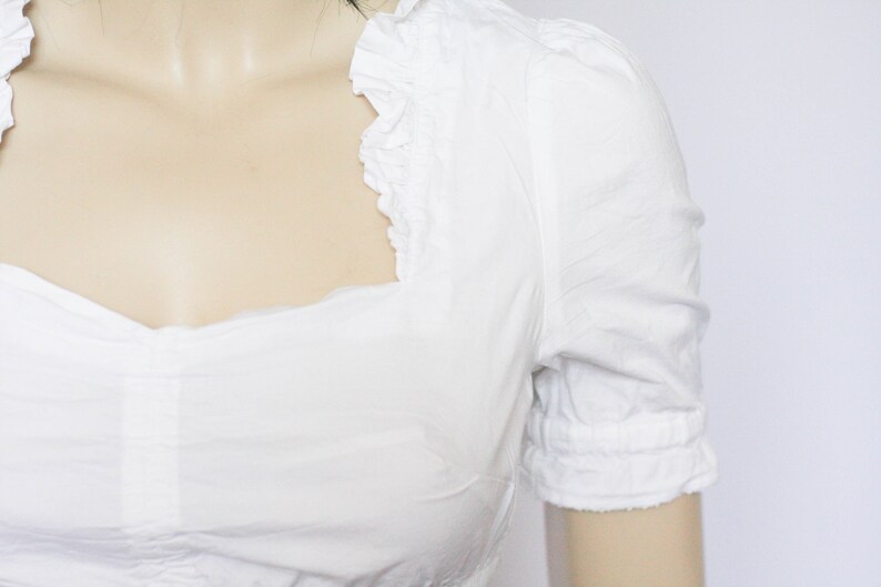 Pu&ograve; includere: Una blusa bianca a maniche corte con scollo a volant.