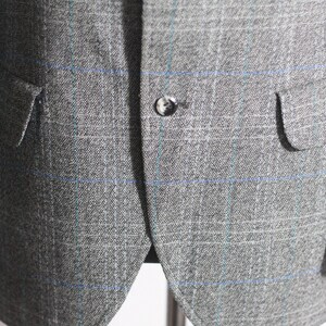Pu&ograve; includere: Un blazer grigio con un motivo a quadri blu e bianchi. Il blazer ha una chiusura con un solo bottone e due tasche a lembo.
