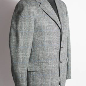 Pu&ograve; includere: Un blazer grigio con un motivo a quadri blu e bianchi. Il blazer ha un risvolto a lancia e tre bottoni.