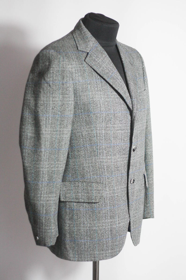 Pu&ograve; includere: Un blazer grigio con un motivo a quadri blu e bianchi. Il blazer ha un risvolto a lancia e tre bottoni.