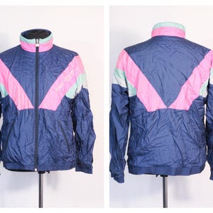 May include: A vintage navy blue track jacket with a full zipper, featuring a pink and mint green chevron design across the chest and back. The jacket has a high collar and a relaxed fit, perfect for casual wear.