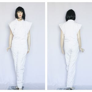 Op de afbeelding: Witte jumpsuit met een rits en korte mouwen. De jumpsuit is gemaakt van een textuur stof.