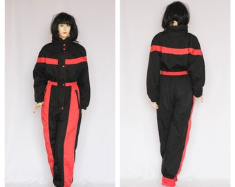 May include: Black and red vintage ski suit. The one-piece snowsuit features a high collar, a red stripe across the chest and waist, and red panels down the legs. The suit has a button-up front and zippered pockets.