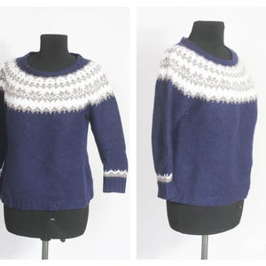 Puede incluir: Un suéter azul marino con un patrón geométrico blanco y gris alrededor del cuello. El suéter tiene mangas largas y cuello redondo.