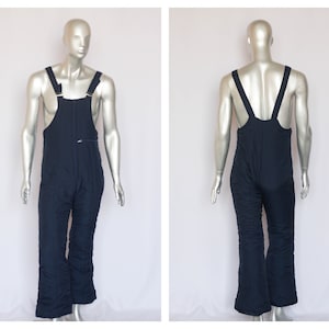 Może przedstawiać: Spodnie robocze w kolorze ciemnoniebieskim, pikowane, z regulowanymi szelkami. Spodnie mają zamek błyskawiczny i luźny krój.