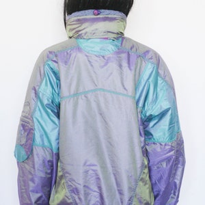 Pu&ograve; includere: Una giacca iridescente viola e turchese con chiusura a zip. La giacca ha un colletto alto e un cordoncino in vita.