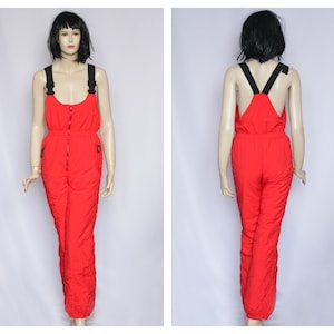 May include: Red ski jumpsuit with black straps and a zipper down the front. The jumpsuit has pockets on the sides and is made of a shiny, nylon-like material.