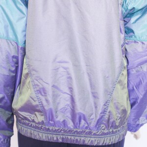 Pu&ograve; includere: Una giacca iridescente viola e blu con chiusura a zip. La giacca ha un design sportivo ed &egrave; realizzata in un materiale leggero.