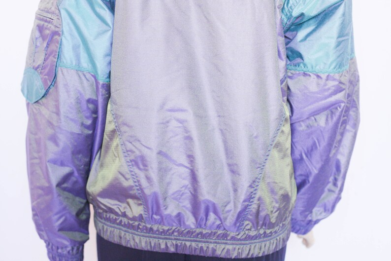Pu&ograve; includere: Una giacca iridescente viola e blu con chiusura a zip. La giacca ha un design sportivo ed &egrave; realizzata in un materiale leggero.