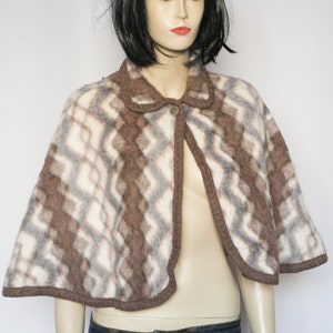 May include: A vintage-style cape in a brown, white, and gray geometric pattern. The cape features a rounded collar and a single button closure. The edges are trimmed with a darker brown fabric. The garment is displayed on a mannequin.