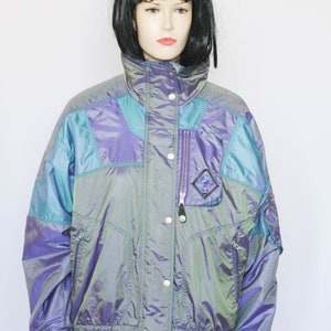 Pu&ograve; includere: Una giacca blu e viola iridescente con chiusura a zip e bottoni a pressione. La giacca ha un colletto alto e una vita con coulisse.