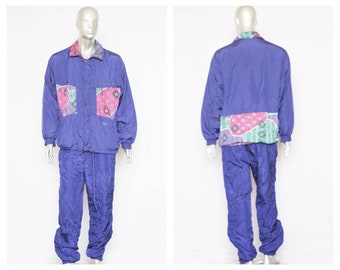 May include: A blue tracksuit with a patterned jacket. The jacket has a geometric pattern in pink, green, and white. The pants are a solid blue color.