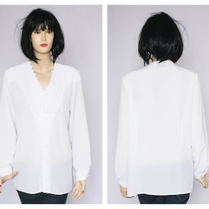 May include: A white long-sleeved blouse with a lace trim around the neckline. The blouse has a button-up front and a relaxed fit.