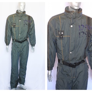 May include: A blue and green plaid ski suit with a black belt and yellow stitching. The suit has a zipper closure and a high collar. The suit has the text "120% 120%" printed on the chest.