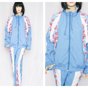 Puede incluir: Un chándal azul con patrones geométricos blancos y rojos. La chaqueta tiene una cremallera y una capucha con cordón. El pantalón tiene una pierna recta.