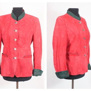 May include: A red suede jacket with a green collar and cuffs. The jacket has a round collar, silver buttons, and two front pockets. The jacket is displayed on a black mannequin.