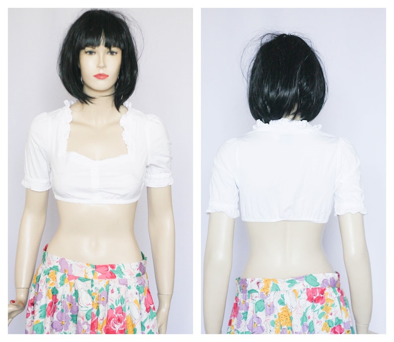 Pu&ograve; includere: Blusa bianca corta con maniche corte e scollo a volant. La blusa &egrave; realizzata in tessuto leggero e ha una vestibilit&agrave; rilassata.