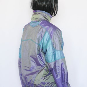 Pu&ograve; includere: Una giacca iridescente viola e turchese con chiusura a zip. La giacca ha un colletto alto e maniche lunghe.