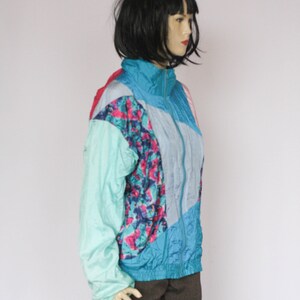Puede incluir: Una chaqueta con estampado azul, rosa y verde con cierre de cremallera. La chaqueta est&aacute; hecha de un material brillante, similar al nylon.
