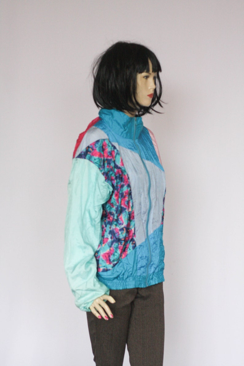 Puede incluir: Una chaqueta con estampado azul, rosa y verde con cierre de cremallera. La chaqueta est&aacute; hecha de un material brillante, similar al nylon.