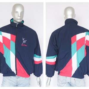 May include: A navy blue jacket with a white, red, and teal geometric pattern. The jacket has a zipper closure and a small embroidered logo on the left chest that says "Grundig".