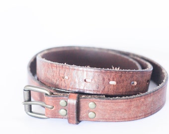 May include: A brown leather belt with a silver buckle and metal rivets. The belt is rolled up and the buckle is visible.