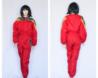 May include: Red ski suit with yellow and green accents. The suit has a zipper down the front and a snap closure at the neck. The suit is made of a shiny, nylon-like material.