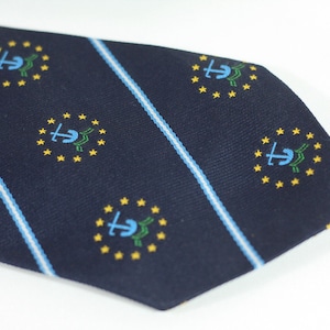 May include: A navy blue tie featuring a repeating pattern of a blue anchor within a green wreath and yellow stars. The tie also has light blue and white stripes. A classic accessory.