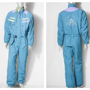 Puede incluir: Un traje de esquí azul con un diseño morado y verde en el pecho y un gráfico blanco en la espalda que dice "Angel of Snow".