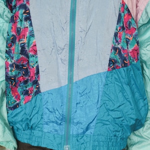 Puede incluir: Una chaqueta vintage multicolor con cierre de cremallera. La chaqueta est&aacute; hecha de un material brillante similar al nailon y presenta un patr&oacute;n geom&eacute;trico en tonos de azul, verde, rosa y blanco.