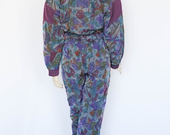 Könnte beinhalten: Ein lila-blauer Ski-Overall mit einem Reißverschluss an der Vorderseite. Der Overall hat einen hohen Kragen und einen Gürtel an der Taille.