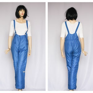 May include: Blue ski overalls with adjustable straps. The overalls have a zipper closure and are made of a shiny, quilted fabric.