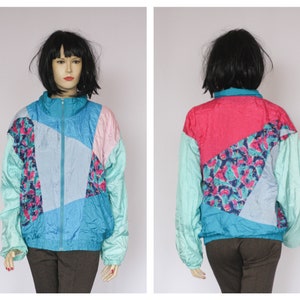 Puede incluir: Una chaqueta cortavientos de color azul, rosa y turquesa con un patr&oacute;n geom&eacute;trico. La chaqueta tiene una cremallera y mangas largas.
