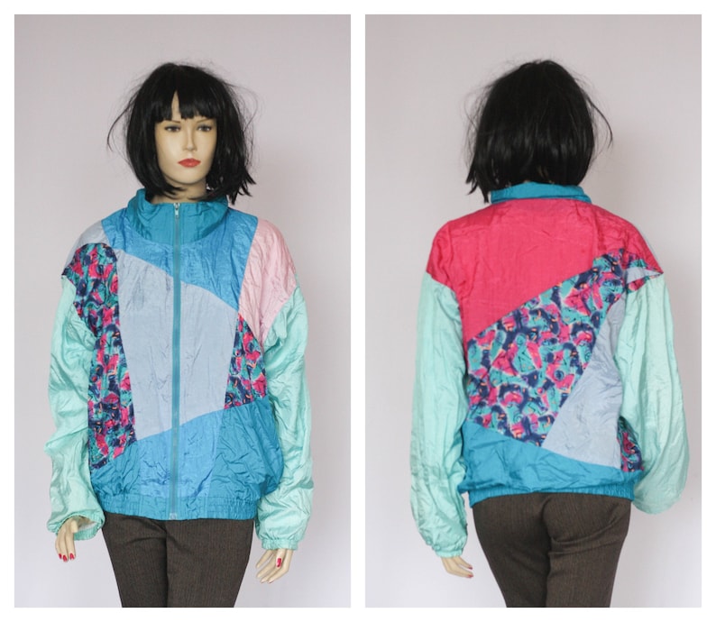 Puede incluir: Una chaqueta cortavientos de color azul, rosa y turquesa con un patr&oacute;n geom&eacute;trico. La chaqueta tiene una cremallera y mangas largas.
