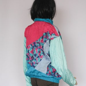 Puede incluir: Una chaqueta cortavientos azul, rosa y turquesa con un patr&oacute;n geom&eacute;trico. La chaqueta tiene una cremallera y un cuello alto.