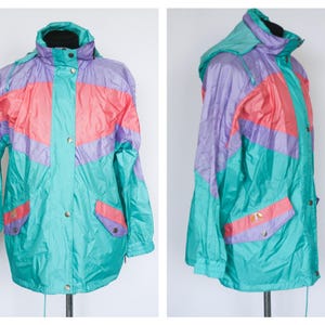May include: A retro colour-blocked jacket in teal, coral, and lavender. The jacket has a hood, snap closures, and pockets. The design is reminiscent of the 1980s with its bold colour scheme and relaxed fit. The jacket is displayed against a white background.