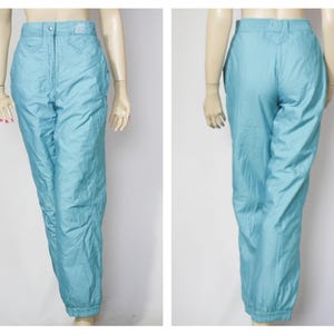Könnte beinhalten: Eine hellblaue Skihose mit hoher Taille und lockerer Passform. Die Hose hat einen Reißverschluss und einen Knopfverschluss und ist aus wasserabweisendem Material gefertigt.