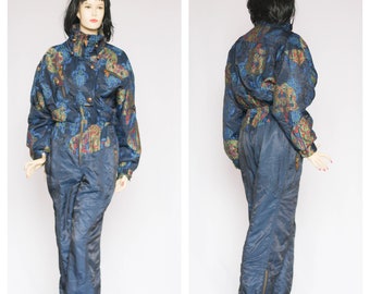 Könnte beinhalten: Ein blauer Ski-Overall mit einem bunten Blumenmuster. Der Overall hat einen Reißverschluss und einen Gürtel.