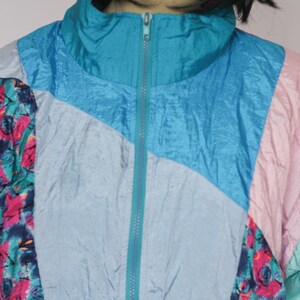Puede incluir: Una chaqueta multicolor con una cremallera turquesa. La chaqueta est&aacute; hecha de un material brillante, similar al nylon, y tiene un patr&oacute;n geom&eacute;trico. La chaqueta est&aacute; en un esquema de color azul claro, turquesa, rosa y blanco.