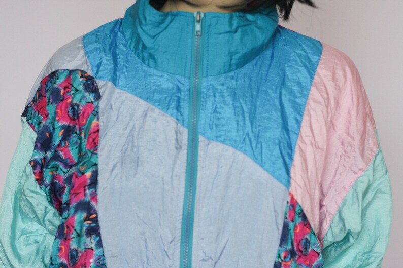 Puede incluir: Una chaqueta multicolor con una cremallera turquesa. La chaqueta est&aacute; hecha de un material brillante, similar al nylon, y tiene un patr&oacute;n geom&eacute;trico. La chaqueta est&aacute; en un esquema de color azul claro, turquesa, rosa y blanco.