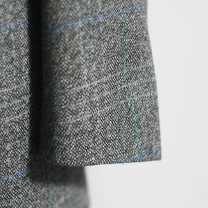 Pu&ograve; includere: Primo piano di un tessuto a quadri grigio e blu con una texture sottile. Il tessuto presenta un motivo intrecciato con sottili linee blu.